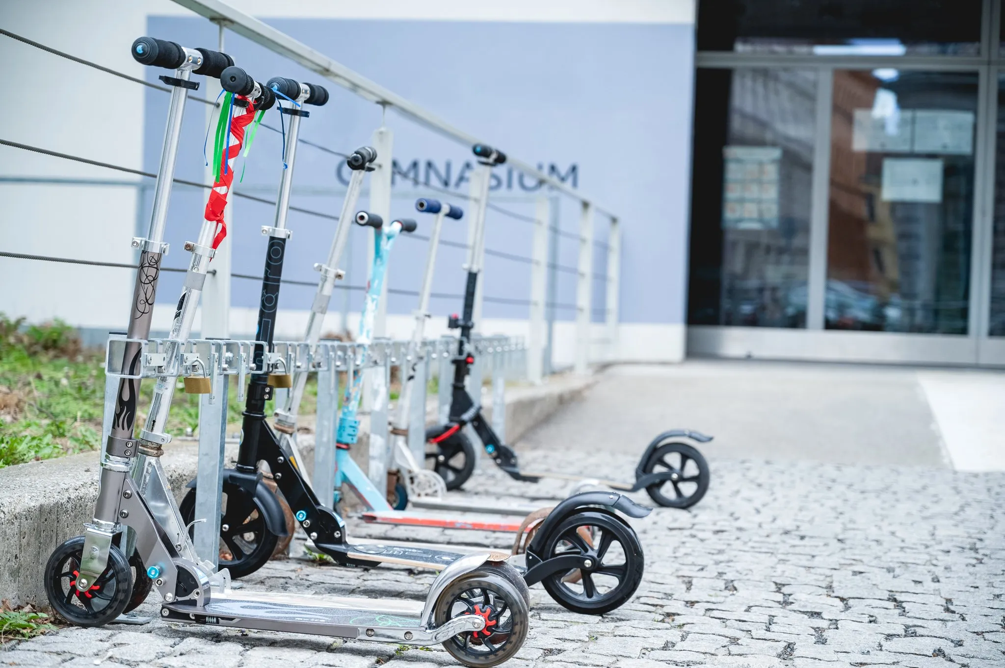 Tretroller mit Vorhängeschlössern in einem Rollerstop RS-Ständer vor einem Gymnasium